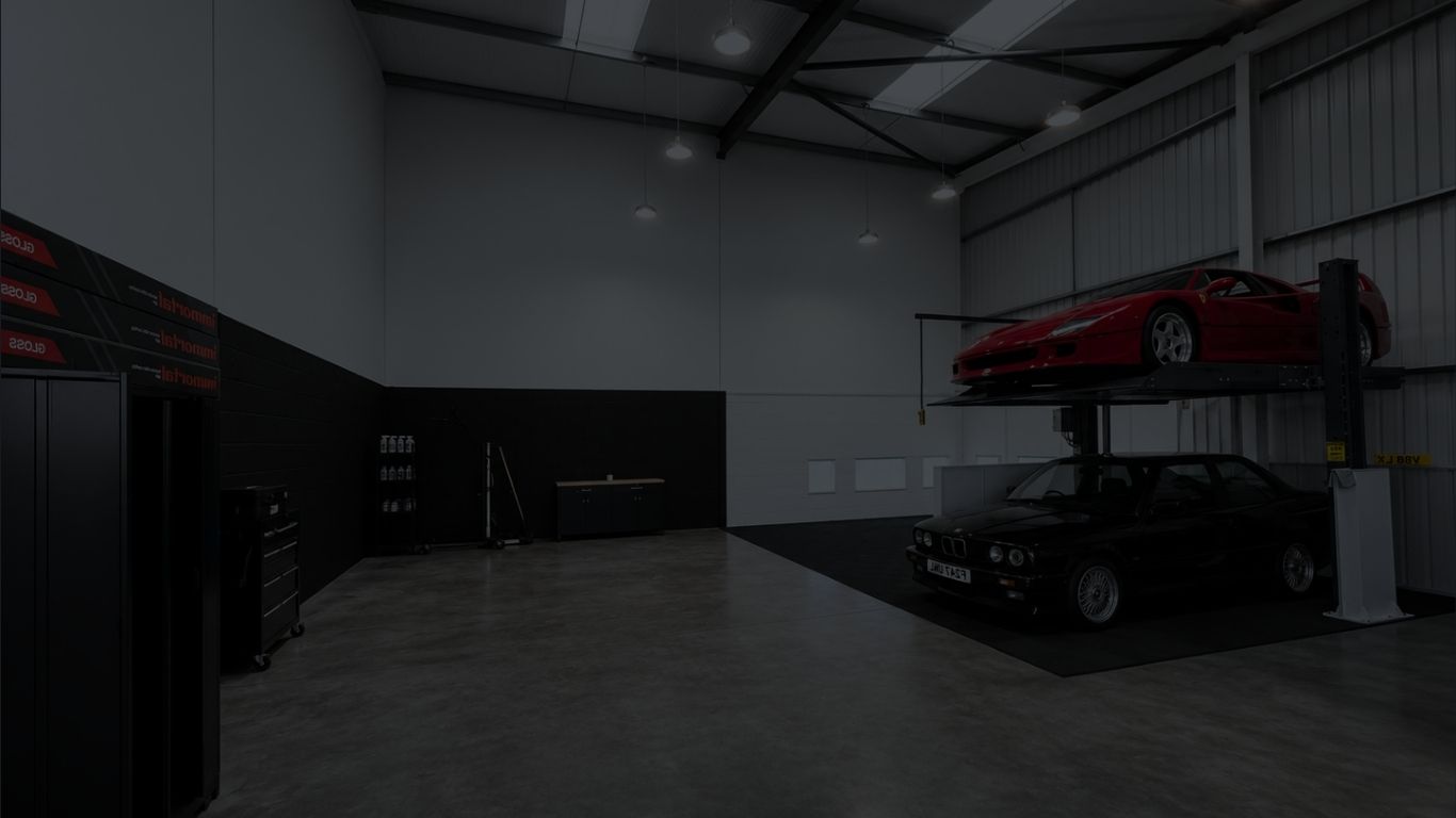 Ferrari raised on a car lift above a BMW inside a dark workshop